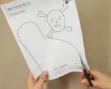 Schere schneidet Vorlage für einen Piratenhut mit Totenkopf. So einfach lässt sich ein Piratenhut basteln!