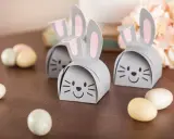 DIY Osternest: Süße Papierhasen mit rosa Ohren und Schokoladeneiern auf Holztisch.