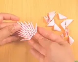 Hände bauen mit rosa Papierstücken ein 3D-Origami-Tier. Die Anleitung ist leicht verständlich.