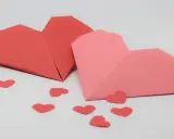 Zwei Origami-Herzen, rot und rosa, umgeben von kleinen roten Herzen. Perfekt zum **Herzen basteln** für den Valentinstag.