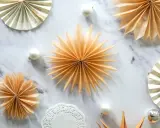 Fächersterne aus Papier, wie bei einer Teebeutel falten Anleitung, schmücken den Marmortisch neben Weihnachtskugeln.