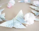 Zarte Origami-Schmetterlinge aus Buchseiten, verziert mit Tupfen und kleinen Papierblumen, bilden einen Kranz. Ein Hauch von origami frühling.