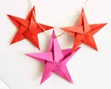 Drei bunte Sterne Origami hängen an einer Schnur. Rote Sterne und ein pinker Stern, perfekt für Weihnachtsdekoration.
