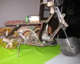 Kreatives Motorrad aus Altmetall, mit einem 50-Euro-Geldschein im Glas als Tank und einem kleinen Motorradhelm-Anhänger.
