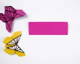 Zwei bunte origami schmetterlinge, einer pink mit Punkten, der andere gelb mit Punkten und Flügelmustern, liegen neben einem Streifen pinken Papiers.