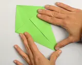 Hände falten ein grünes Papier, um einen einfachen Drachen zu basteln.