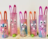 Fünf bunte Osterhasen aus Klopapierrollen mit großen Augen und rosa Ohren, dekoriert mit Pinselstrichen.