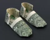 Zwei kunstvoll gefaltete Schuhe aus Geldscheinen, die wie kleine Ballerinas aussehen.