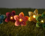 Bunte Papierblumen leuchten auf grünem Gras. Eine selbstgebastelte Lichterkette, die Kinder lieben werden.