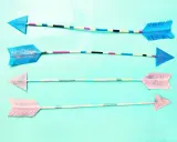 Vier bunte Pfeile zum Basteln, mit Glitzer verziert und auf hellblauem Hintergrund arrangiert.