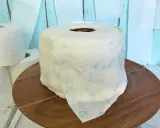 Eine Torte aus Toilettenpapier basteln: Ein realistisch aussehender Kuchen in Form einer Toilettenpapierrolle, verziert mit blauen Blumenmustern.