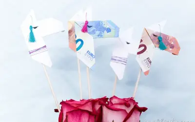 Origami-Pferde aus Geld gefaltet, mit bunten Quasten und Rosen. Ein kreatives Geldgeschenk.