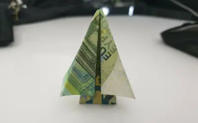 Ein kleiner, gefalteter Baum aus Geldscheinen steht auf einem Tisch. Ein kreativer geld falten baum.
