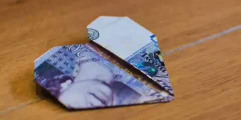 Ein Herz aus gefalteten Geldscheinen liegt auf Holz. Die Noten zeigen die Zahl 20.