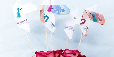 Origami-Pferde aus Geld gefaltet, mit bunten Quasten und Rosen. Ein kreatives Geldgeschenk.