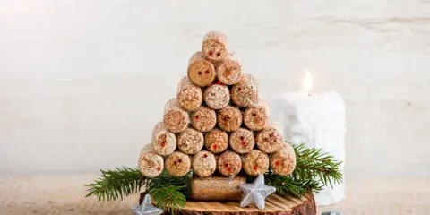 Weihnachtsbaum aus Korken, ein tolles Bastelprojekt für Erwachsene. Mit Tannenzweigen und Sternen dekoriert, neben einer Kerze.