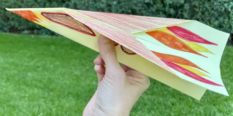 Bunter Papierflieger mit Flammenmuster, bereit zum Abheben. Hier ist die papierflieger anleitung zum ausdrucken.
