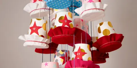 Bunte Becher mit Sternen und Punkten, die als Adventskalender becher basteln dienen. Jede Tasse hat eine Zahl und eine Stoffkappe.