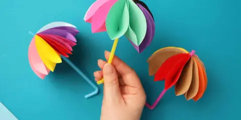 Bunte Regenschirme aus Tonpapier, perfekt zum Basteln mit Kindern. Ein gelber Schirm wird von einer Hand gehalten.
