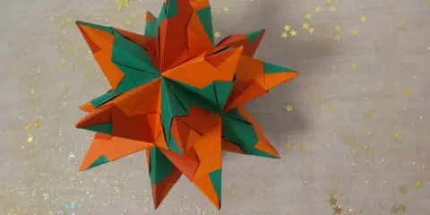 Ein sternförmiges Origami-Objekt in Orange und Grün, das an einen funkelnden Winterhimmel erinnert.
