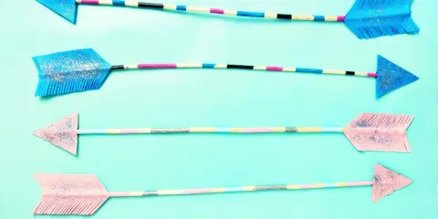 Vier bunte Pfeile zum Basteln, mit Glitzer verziert und auf hellblauem Hintergrund arrangiert.