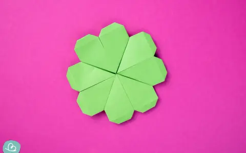 Ein grüner Origami-Glücksbringer, der wie ein Kleeblatt aussieht, auf einem pinken Hintergrund.