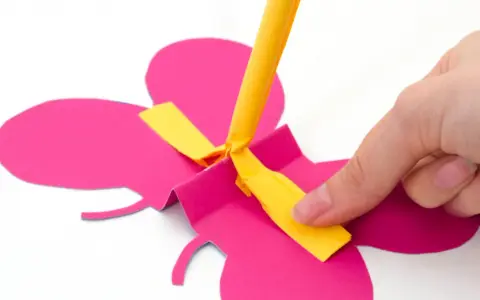 Hand bastelt fliegende Schmetterlinge aus pinkem Papier. Ein gelber Streifen wird befestigt.
