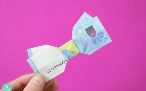 Ein 20-Euro-Schein ist zu einer Schleife gefaltet. Ein Finger hält das gefaltete Geld.