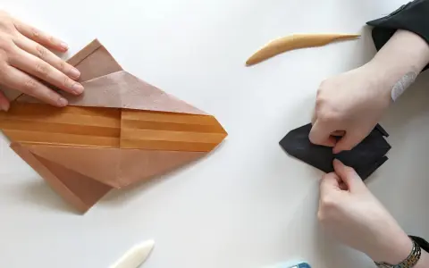 Zwei Hände falten Papier, eine an einem komplexen braunen Origami, die andere an einem schwarzen. Eine schwierige Origami-Anleitung wird befolgt.