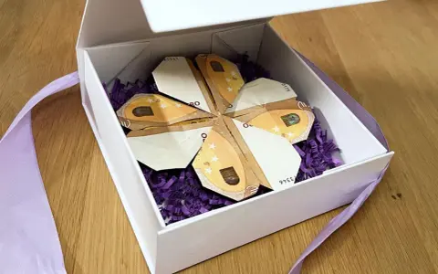 Ein Geschenk: Geld falten blatt in Form eines Kleeblatts, liebevoll in einer weißen Schachtel mit lila Füllung und Band arrangiert.