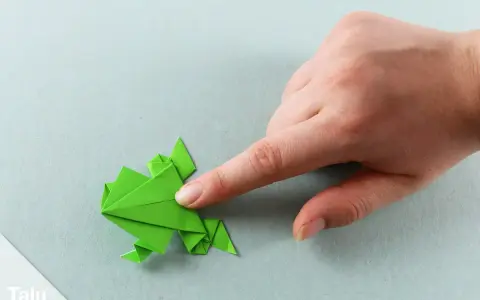 Grüner Origami-Frosch wird von einer Hand geformt. Eine einfache origami vorlage zum Nachfalten.