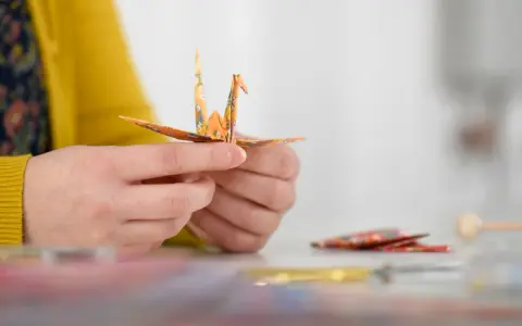 Hände falten einen Kranich aus buntem Papier. Ein schöner Moment während eines Origami Kurses.