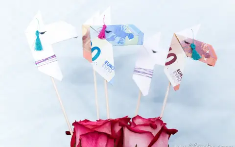 Origami-Pferde aus Geld gefaltet, mit bunten Quasten und Rosen. Ein kreatives Geldgeschenk.