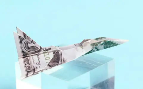 Ein **Flugzeug aus Geld falten** ist ein Kunstwerk. Ein Dollar-Schein wurde zu einem Jet gefaltet, der auf einem transparenten Block thront.