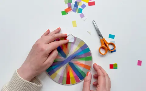 Hände basteln mit transparentsterne falten, bunte Streifen auf einem Kreis, daneben Schere und Konfetti.