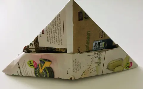 Ein dreieckiger Papierhut, gefaltet aus Zeitungspapier mit Werbung für Käse und Kaffee. Das Papierhut falten ist eine einfache Bastelidee.