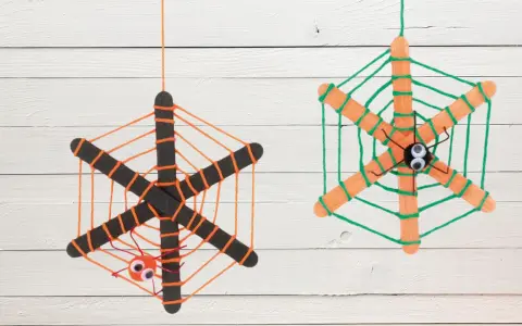 Zwei selbstgebastelte Spinnennetze aus Eisstielen und Wolle, mit kleinen Spinnen und Kulleraugen. Perfekt zum Spinnennetz basteln für Halloween!