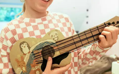 Kind bastelt Gitarre nach Vorlage. Die selbstgemachte Gitarre ist mit süßen Tieren wie Pinguin, Panda, Hase und Fuchs bemalt.