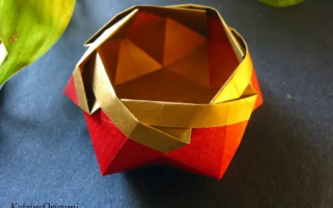 Eine kunstvolle origami schale in Rot und Gold, daneben ein grünes Blatt.