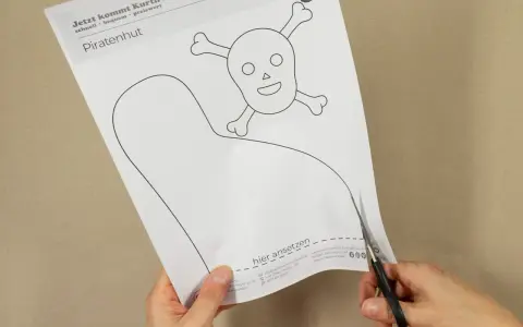 Schere schneidet Vorlage für einen Piratenhut mit Totenkopf. So einfach lässt sich ein Piratenhut basteln!