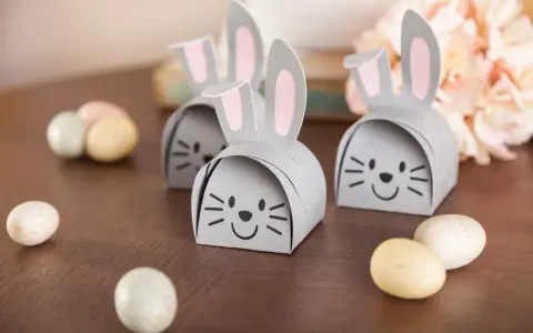 DIY Osternest: Süße Papierhasen mit rosa Ohren und Schokoladeneiern auf Holztisch.