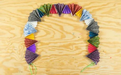 Bunte Papierfächer, die zu einer ziehharmonika-girlande gebastelt wurden, liegen auf einer Holzplatte.