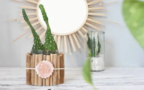 Zwei Kakteen in einem selbstgemachten Blumentopf aus Holzstäbchen. Ein Schild mit "STAY ALIVE" hängt daran.