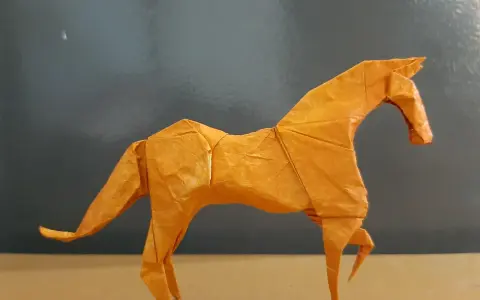 Ein orangefarbenes Origami-Pferd steht auf einem Tisch.