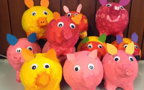 Bunte Pappmaché-Sparschweine mit großen Kulleraugen und Papierohren stehen fröhlich nebeneinander.