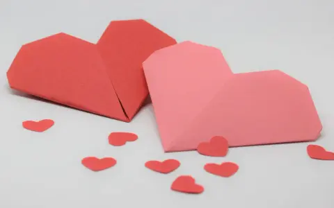 Zwei Origami-Herzen, rot und rosa, umgeben von kleinen roten Herzen. Perfekt zum **Herzen basteln** für den Valentinstag.
