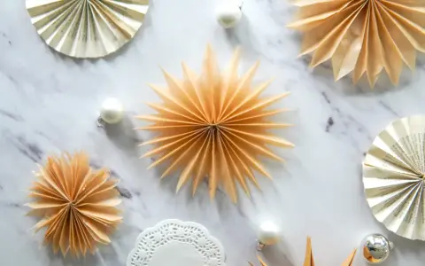 Fächersterne aus Papier, wie bei einer Teebeutel falten Anleitung, schmücken den Marmortisch neben Weihnachtskugeln.