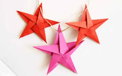 Drei bunte Sterne Origami hängen an einer Schnur. Rote Sterne und ein pinker Stern, perfekt für Weihnachtsdekoration.