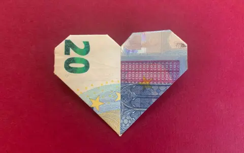 Ein gefaltetes Herz aus 20-Euro-Scheinen auf rotem Untergrund.