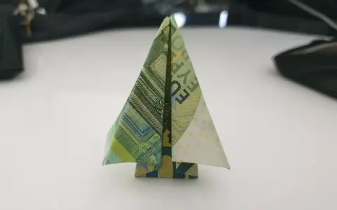 Ein kleiner, gefalteter Baum aus Geldscheinen steht auf einem Tisch. Ein kreativer geld falten baum.